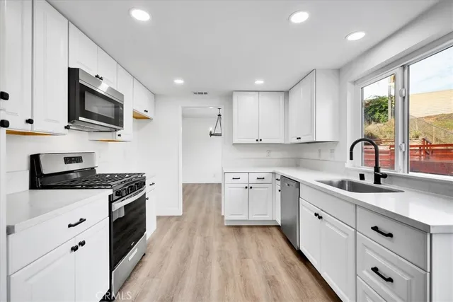 a kitchen with stainless steel appliances granite countertop a sink dishwasher stove and white cabinets with wooden floor