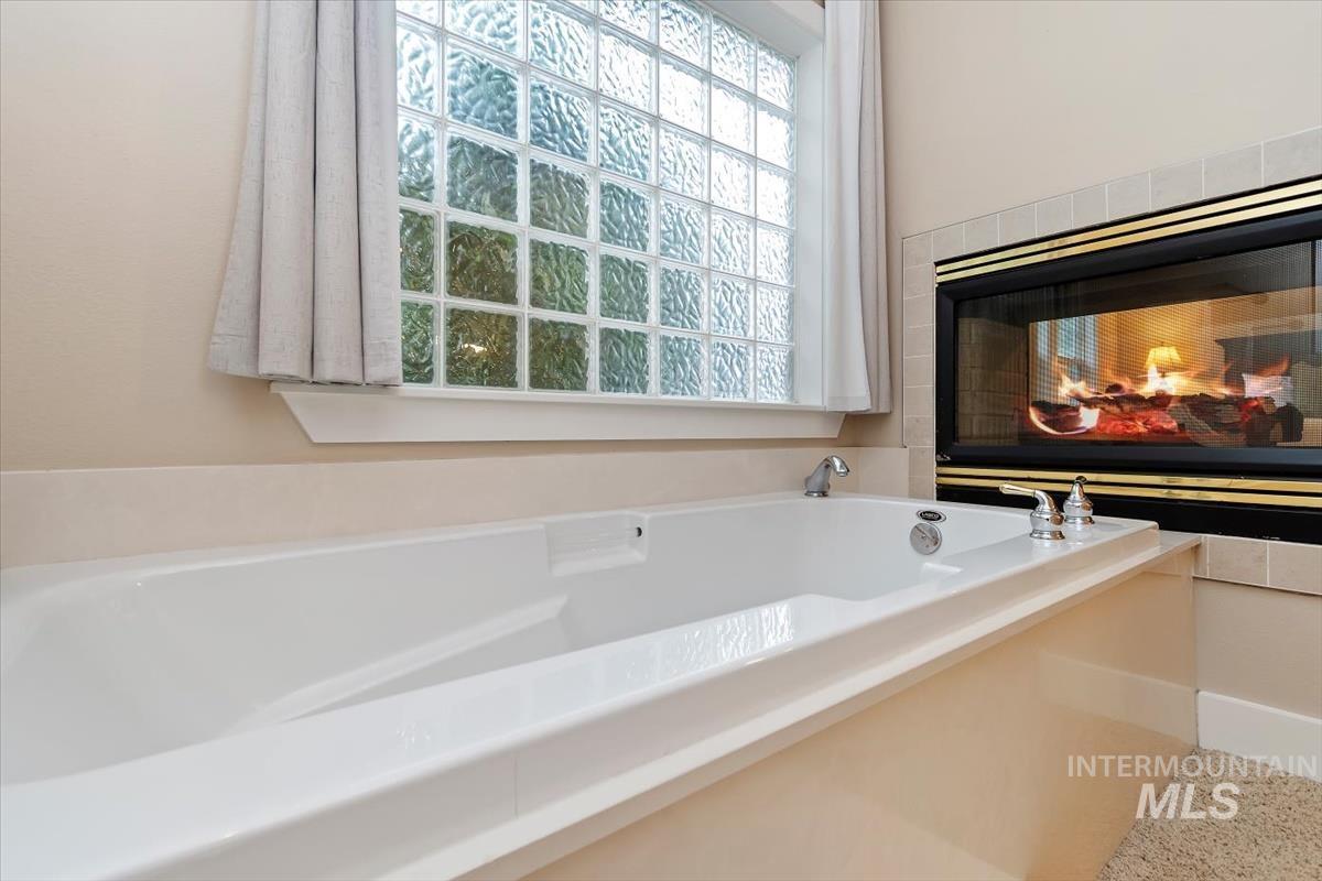 10462 West Lanktree Gulch Road Star, ID 83669 - Photo 20 of 48 Built-in soaking tub featuring deck-mounted fixtures, a glass block window with privacy curtain, and a tiled fireplace surround with a glass-front fireplace
