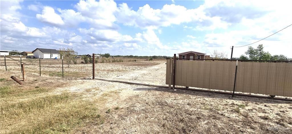 189 Midway Road Rio Grande City, TX 78582 - Photo 3 of 20 Expansive open land with a gravel drive, partial wire fencing, and a large privacy gate