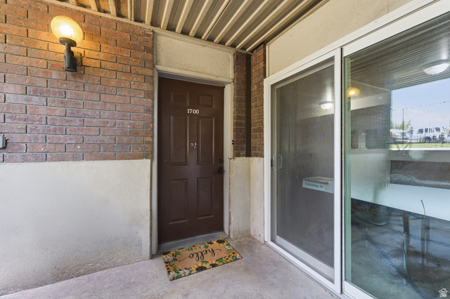 1700 Hickory Lane Provo, UT 84604 - Photo 8 of 20 Brick exterior with an entryway sconce, a paneled brown door, and adjacent sliding glass doors