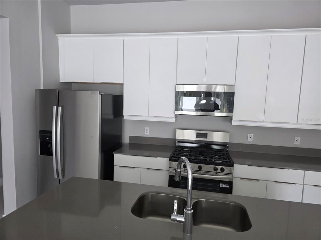 7760 Sandy Ridge Drive, Unit 112 Reunion, FL 34747 - Photo 4 of 23 a kitchen with stainless steel appliances a refrigerator a stove a sink and white cabinets