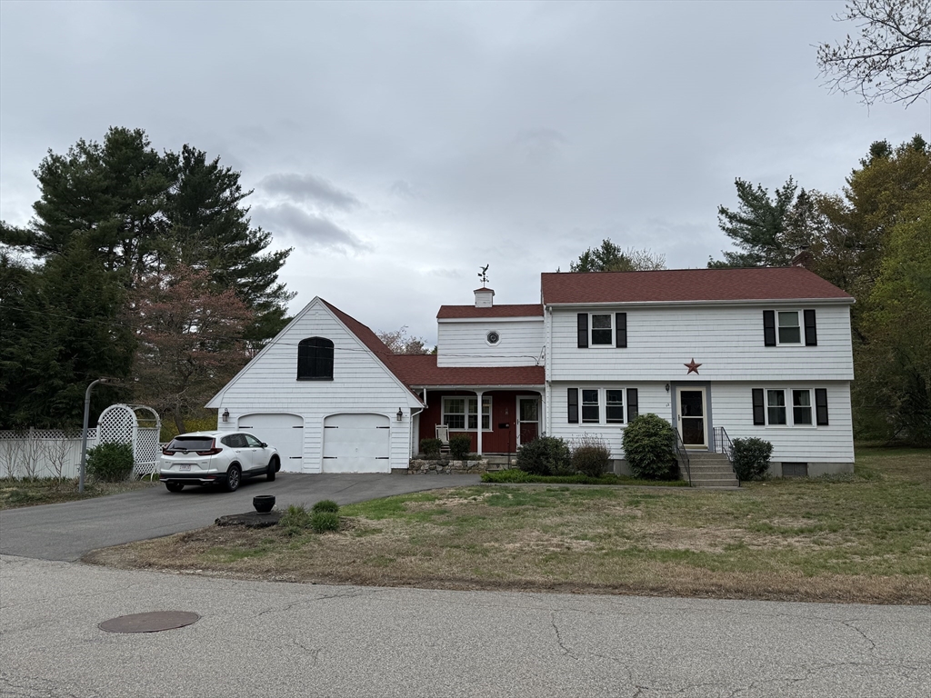 a view of a white house next to a yard with road and trees