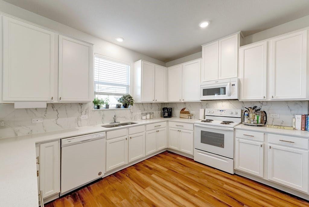13916 Inaugural Street Manor, TX 78653 - Photo 6 of 28 A well-appointed kitchen features white cabinetry, marble-patterned backsplash, and rich hardwood flooring.