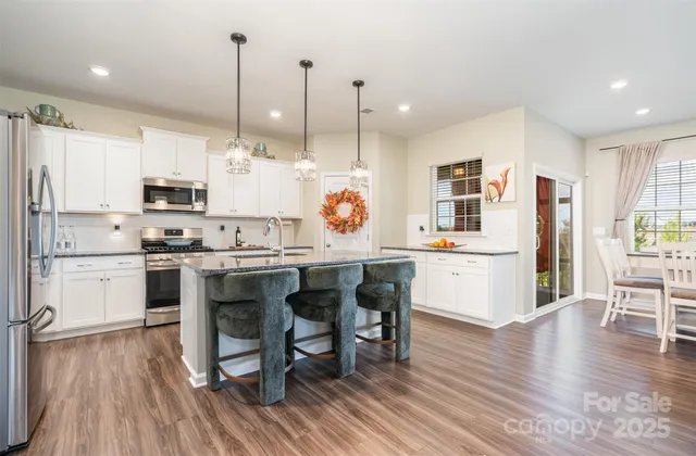 a kitchen with stainless steel appliances granite countertop a refrigerator a stove top oven a sink dishwasher and white cabinets with wooden floor