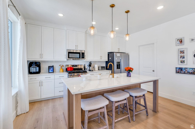 2664 West Maple Street Mapleton, UT 84664 - Photo 14 of 49 Bright kitchen featuring white shaker cabinetry, stainless steel appliances, a white subway tile backsplash, a central island with a light-toned wood base and a white countertop, and three glass pendant lights