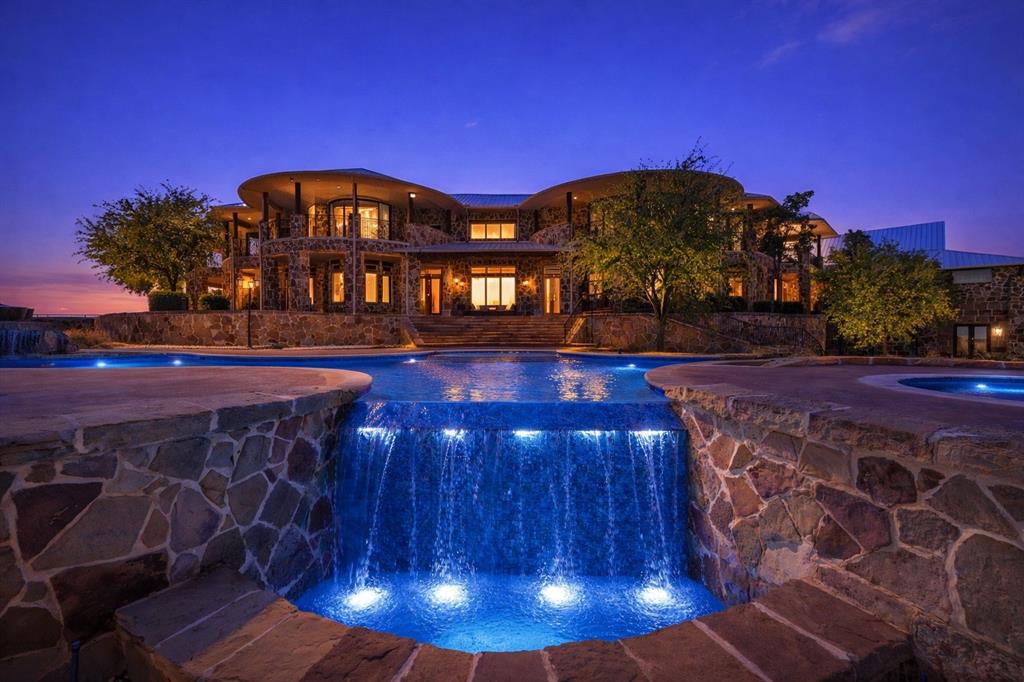 1180 McReynolds Road Sanger, TX 76266 - Photo 34 of 40 Expansive multi-level stone residence featuring a large water feature with integrated lighting, multiple swimming pools, and a stone patio