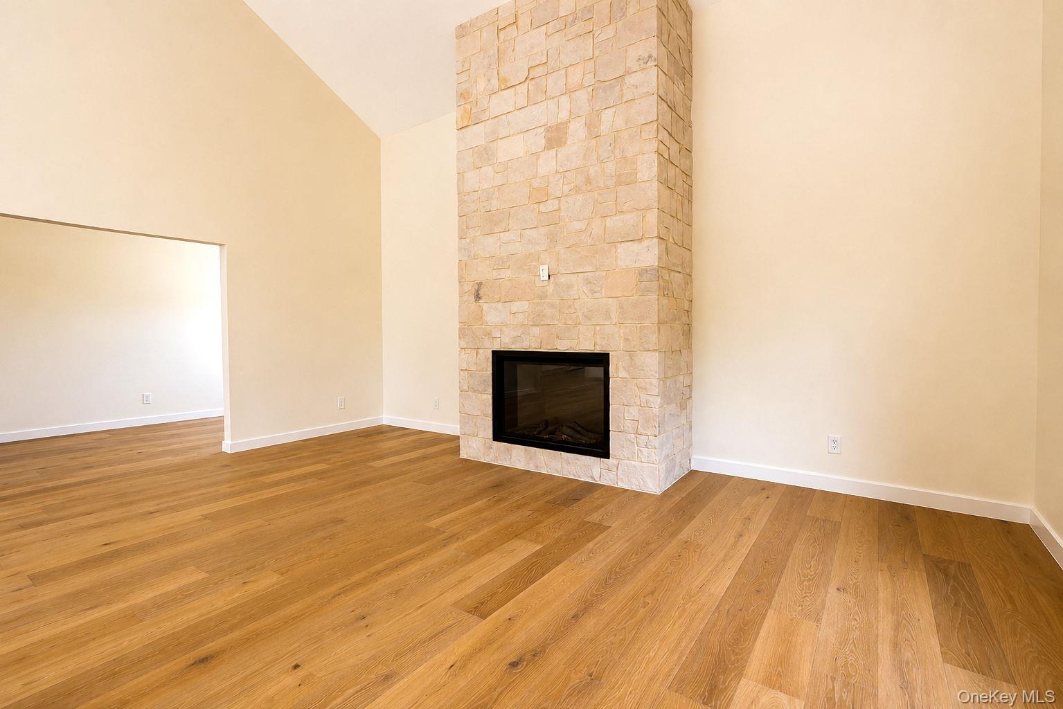 128 St Elmo Road Wallkill, NY 12589 - Photo 15 of 45 Spacious room featuring a floor-to-ceiling stone fireplace with a black insert, vaulted ceiling, wood-finish flooring, and access to office/den on left.