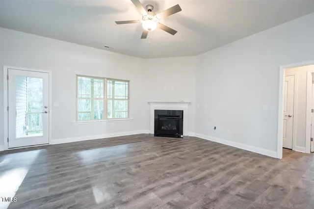 a view of an empty room with wooden floor fireplace and a window