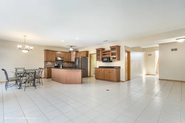 a kitchen with stainless steel appliances granite countertop a stove top oven a refrigerator a kitchen island and chairs