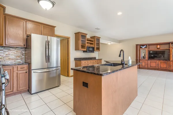 a kitchen with stainless steel appliances kitchen island granite countertop a refrigerator a stove a sink and white cabinets with wooden floor