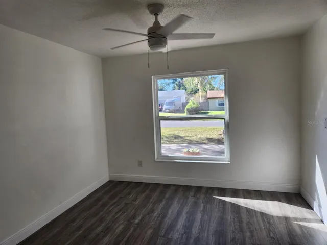 an empty room with wooden floor fan and windows
