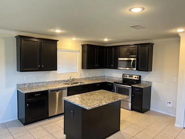 a kitchen with stainless steel appliances granite countertop a stove top oven a sink dishwasher and a refrigerator with wooden cabinets