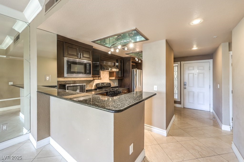 270 East Flamingo Road, Unit 115 Las Vegas, NV 89169 - Photo 8 of 29 Kitchen featuring light tile patterned flooring, dark stone countertops, black appliances, dark brown cabinetry, and wall chimney range hood