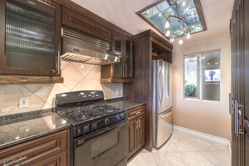 270 East Flamingo Road, Unit 115 Las Vegas, NV 89169 - Photo 9 of 29 Kitchen featuring black gas range, dark brown cabinets, exhaust hood, dark stone counters, and freestanding refrigerator