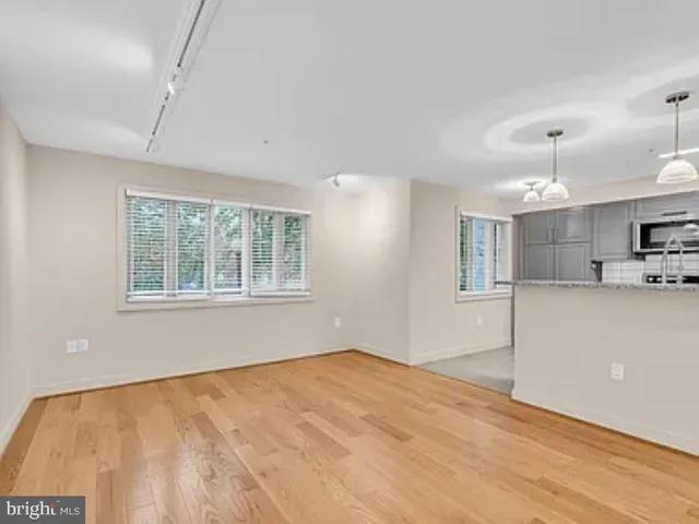 a view of an empty room with kitchen and window