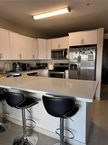 a kitchen with stainless steel appliances a refrigerator a sink a stove a microwave a refrigerator and chairs