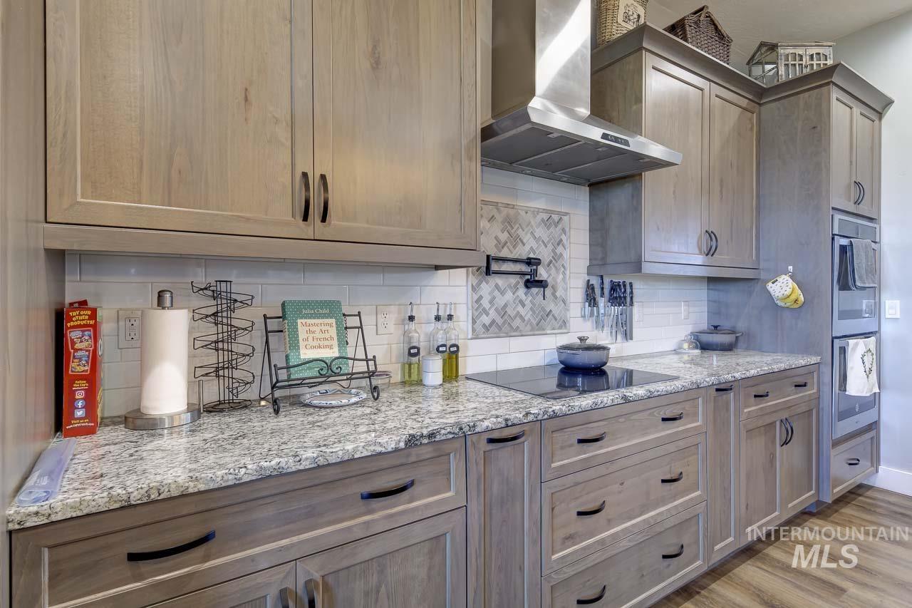 415 North Locust Grove Road Kuna, ID 83634 - Photo 14 of 49 Kitchen featuring wall chimney range hood, backsplash, light stone countertops, double oven, and light wood finished floors