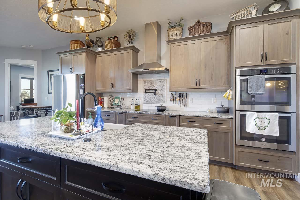 415 North Locust Grove Road Kuna, ID 83634 - Photo 17 of 49 Kitchen with appliances with stainless steel finishes, wall chimney range hood, light stone countertops, and decorative backsplash