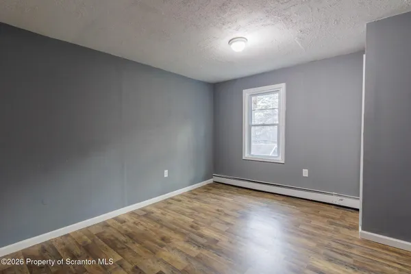 a view of an empty room with wooden floor and window