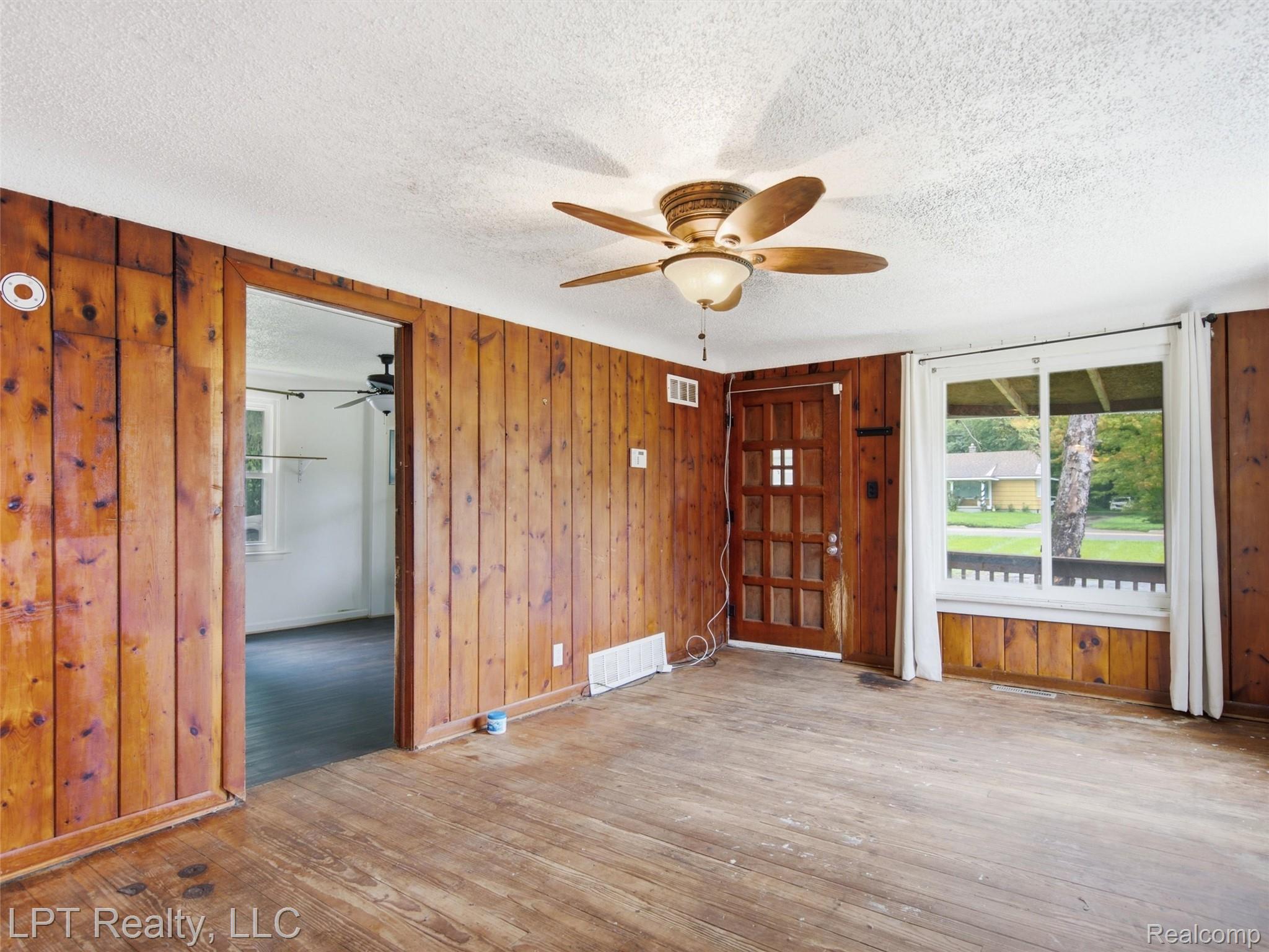 Wood-paneled interior walls, wood-finish flooring, white ceiling, and a ceiling fan with integrated lighting