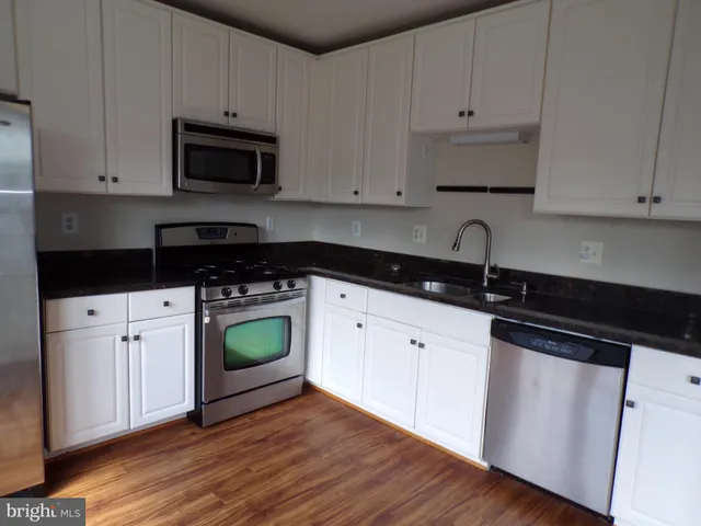 a kitchen with granite countertop white cabinets and black appliances with wooden floor