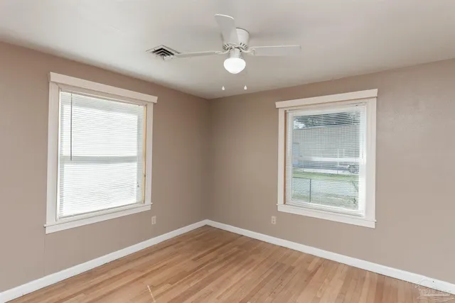 an empty room with wooden floor fan and windows