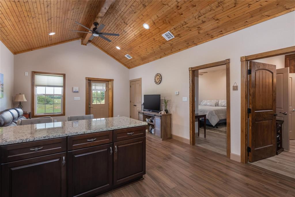 210 Spring Branch Trail North Springtown, TX 76082 - Photo 7 of 36 Open-concept living space featuring a granite-topped island with storage, wood-finish flooring, and a vaulted tongue-and-groove wood ceiling with exposed beam accents