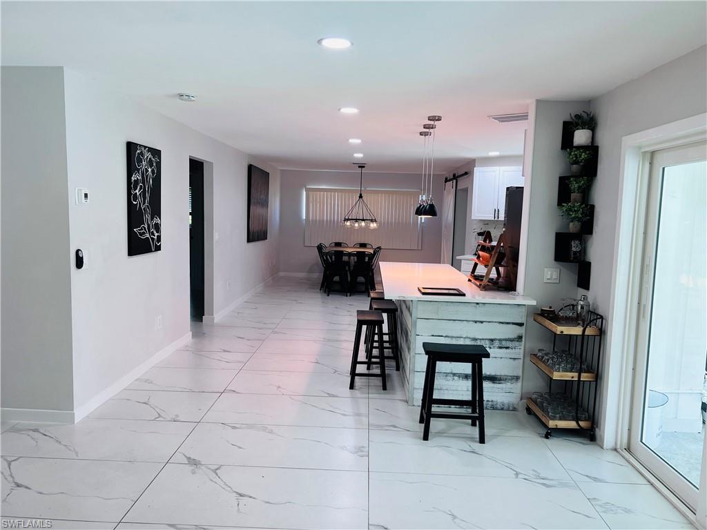 4439 Parrot Avenue Naples, FL 34104 - Photo 12 of 14 Kitchen with a kitchen bar, decorative light fixtures, a peninsula, white cabinetry, and light marble finish floors