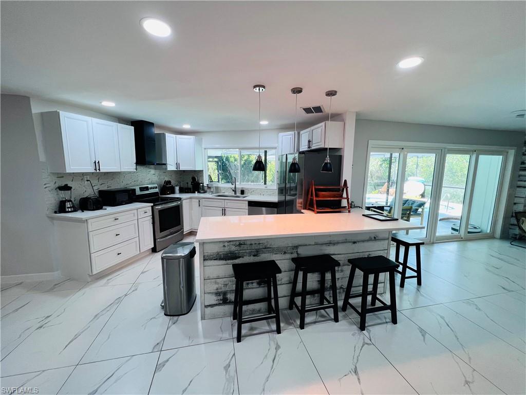 4439 Parrot Avenue Naples, FL 34104 - Photo 2 of 14 Kitchen with white cabinetry, black appliances, a breakfast bar area, pendant lighting, and a peninsula