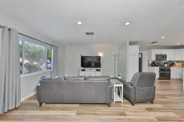 a living room with couches a flat screen tv and kitchen view with wooden floor