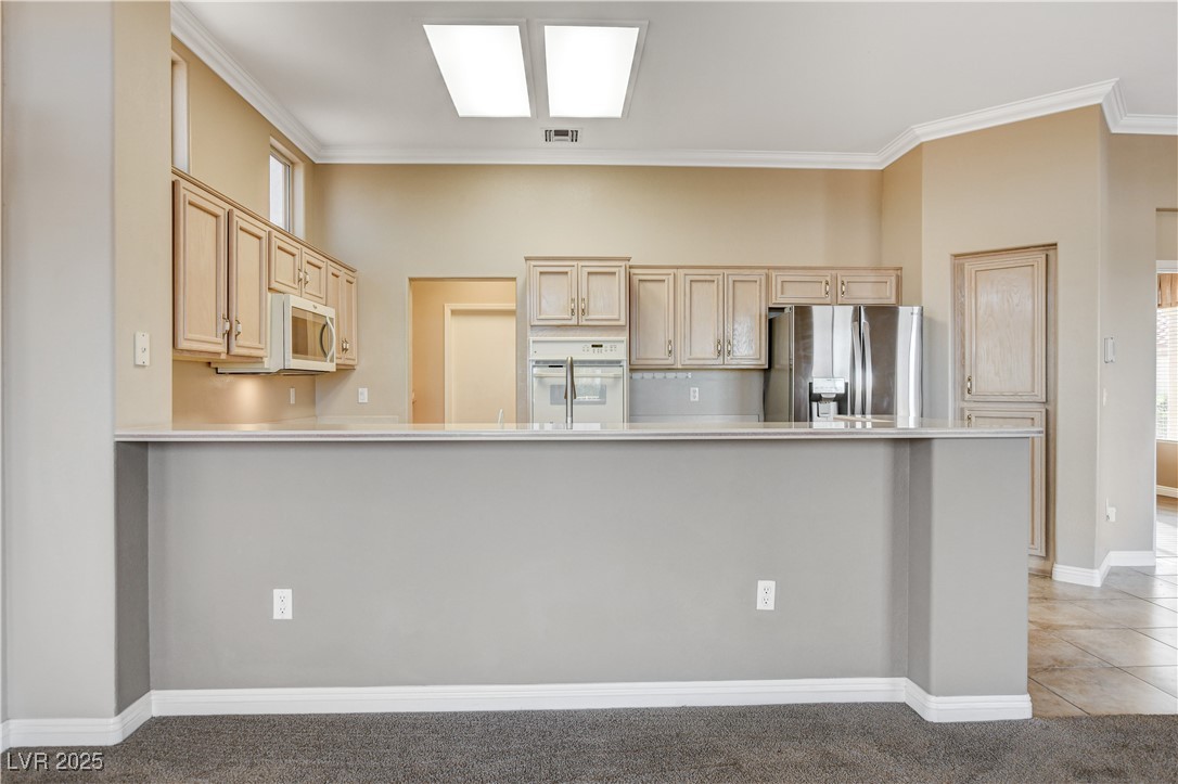 1904 Hot Oak Ridge Street Las Vegas, NV 89134 - Photo 21 of 74 Kitchen with light countertops, white appliances, ornamental molding, light brown cabinetry, and light colored carpet