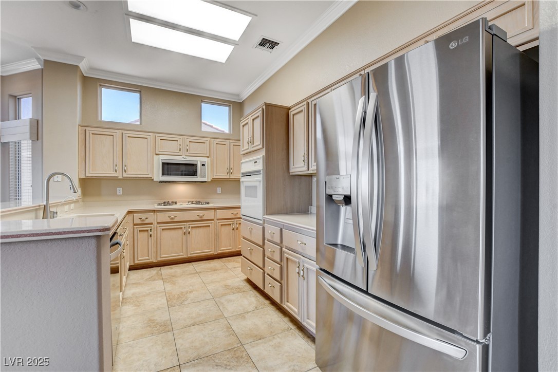 1904 Hot Oak Ridge Street Las Vegas, NV 89134 - Photo 22 of 74 Kitchen with appliances with stainless steel finishes, light countertops, light brown cabinetry, ornamental molding, and light tile patterned floors