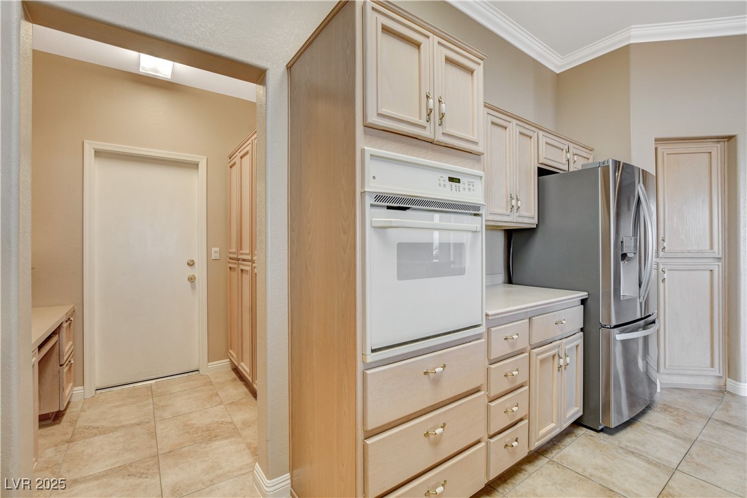 1904 Hot Oak Ridge Street Las Vegas, NV 89134 - Photo 26 of 74 Kitchen featuring white oven, light countertops, light tile patterned flooring, crown molding, and stainless steel fridge