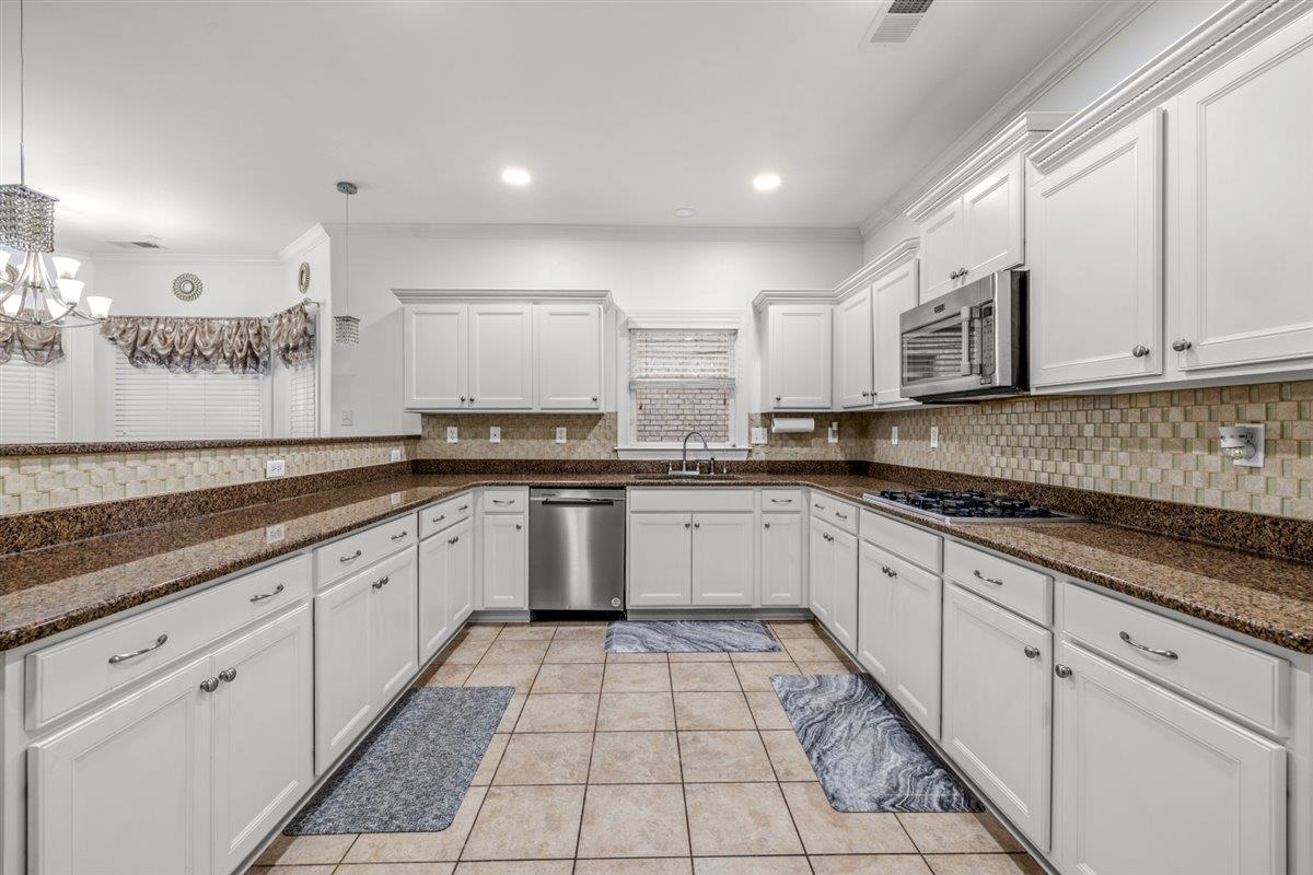 744 Southern Home Road Collierville, TN 38017 - Photo 13 of 24 U-shaped kitchen with white cabinetry, stainless steel appliances, dark stone countertops, and tile backsplash