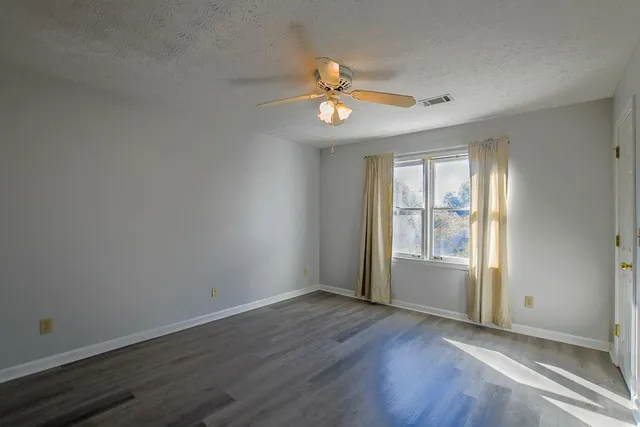 an empty room with wooden floor fan and windows