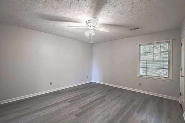 an empty room with wooden floor fan and windows
