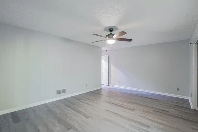a view of an empty room with a chandelier fan and wooden floor