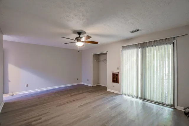 an empty room with wooden floor fan and windows