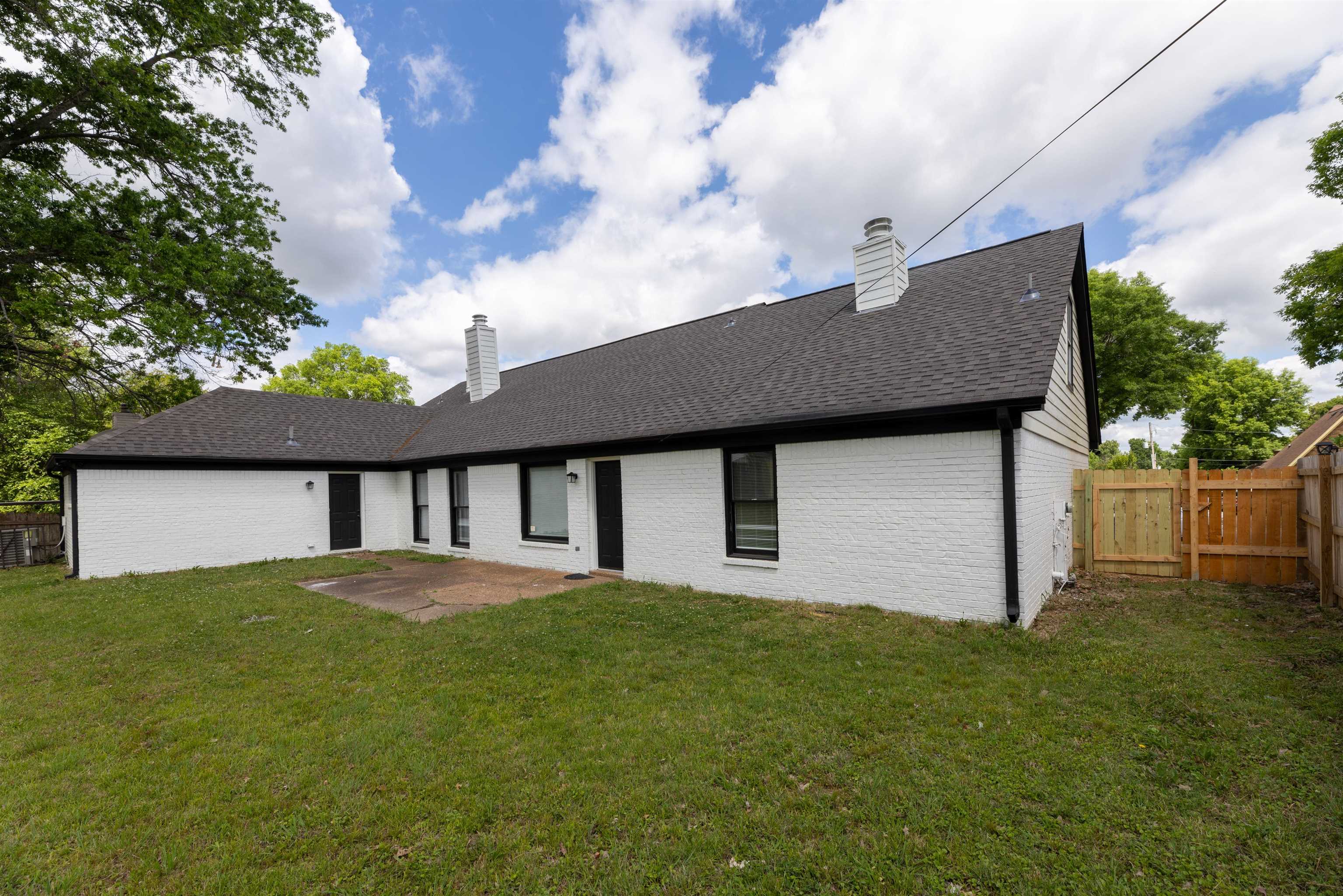 7421 Richmond Road Memphis, TN 38125 - Photo 39 of 39 Expansive backyard featuring a manicured lawn, white brick exterior, black trim windows, a concrete patio, and a wood privacy fence