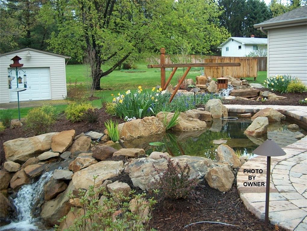 676 Deer Creek Road Valencia, PA 16059 - Photo 22 of 25 This Spring photo shows flowers in bloom around the beautiful pavers patio with two more water features leading to the flat, large back yard. The garage to the left can be used to house tractors, quads, etc.