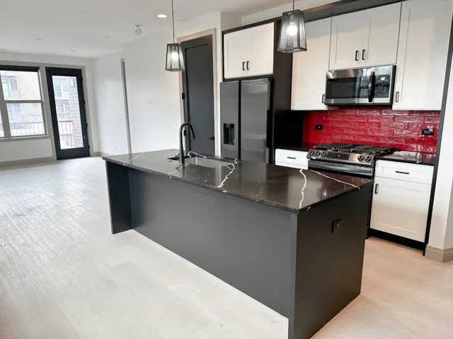 a kitchen with stainless steel appliances granite countertop a refrigerator a sink dishwasher a stove and a dining table with wooden floor