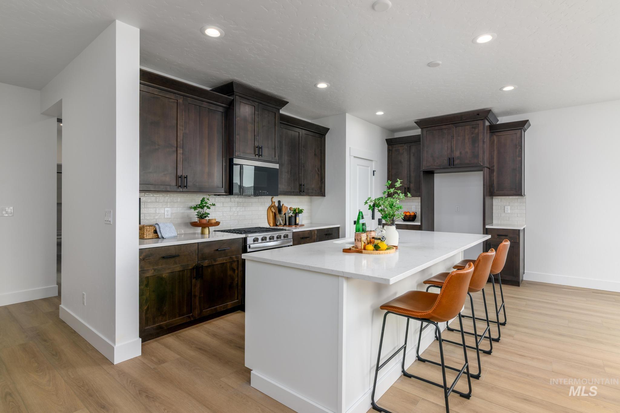 1745 West Arya Street Kuna, ID 83634 - Photo 3 of 11 Kitchen featuring a breakfast bar, light wood-style floors, decorative backsplash, light stone counters, and stainless steel range with gas cooktop