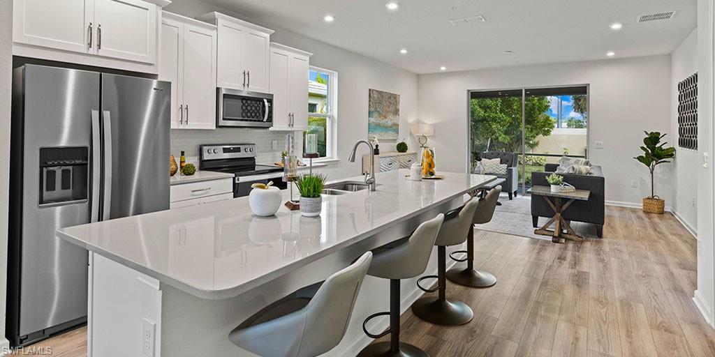 4653 Arboretum Circle, Unit 104 Naples, FL 34112 - Photo 4 of 21 a kitchen with stainless steel appliances kitchen island granite countertop a table chairs refrigerator and microwave