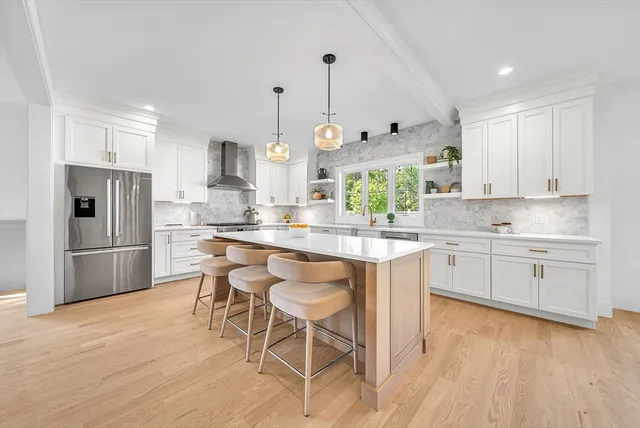 a kitchen with stainless steel appliances granite countertop a refrigerator a sink dishwasher a stove a dining table and chairs with wooden floor
