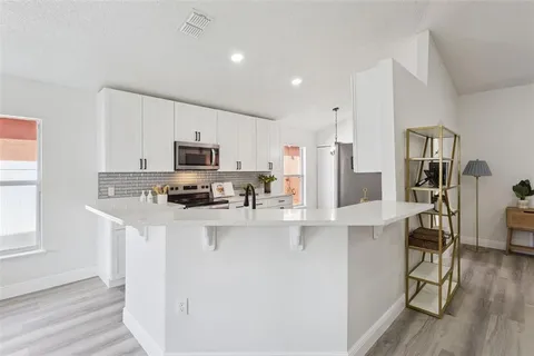 a kitchen with stainless steel appliances granite countertop a refrigerator a stove top oven a sink dishwasher and white cabinets with wooden floor