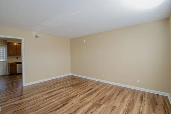 a view of an empty room with wooden floor and a kitchen