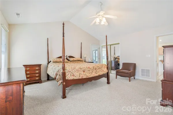 a bedroom with a bed a chair and potted plant on the dresser