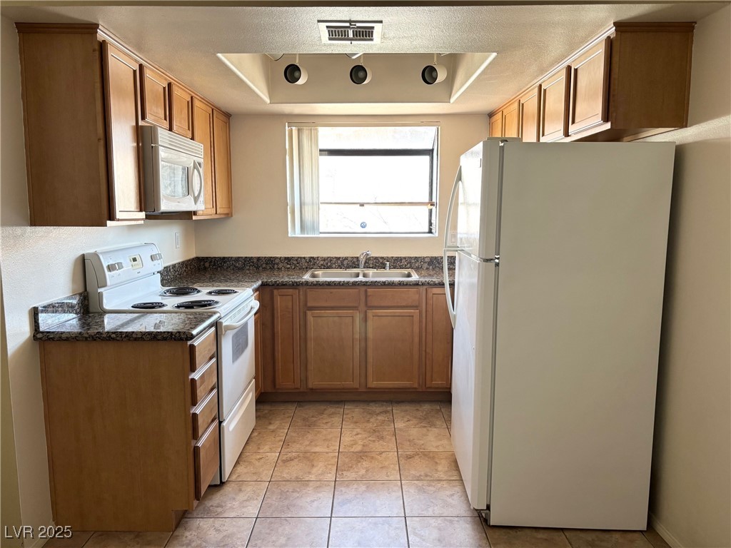 7300 West Pirates Cove Road, Unit 2054 Las Vegas, NV 89145 - Photo 4 of 16 Kitchen featuring white appliances, a sink, a tray ceiling, and dark countertops