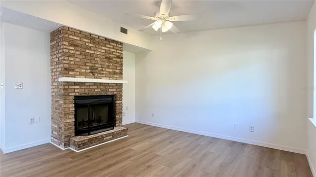 a view of a livingroom with a fireplace a ceiling fan and wooden floor
