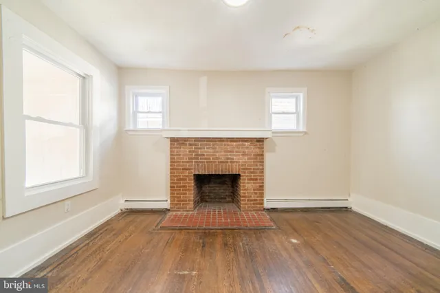 an empty room with wooden floor fireplace and windows
